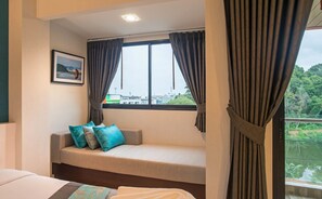 Una habitación con cama, ventana con cortinas, sofá con cojines y un cuadro en la pared.