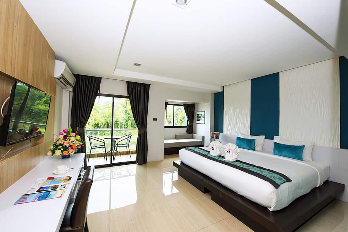 Habitación de hotel moderna con una cama grande, un escritorio con una silla, televisión y un balcón con vistas a zonas verdes.