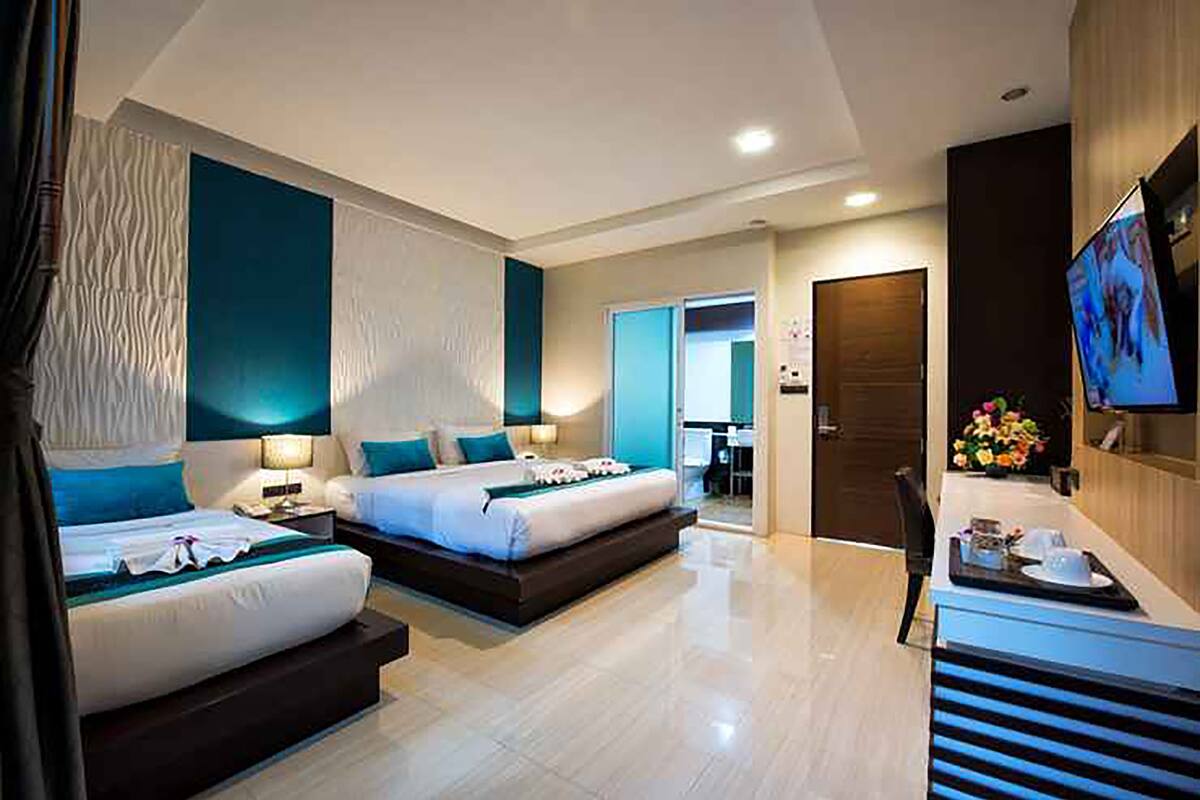 Una habitación de hotel moderna con dos camas, un escritorio con una silla, un televisor y un baño a la vista al fondo.