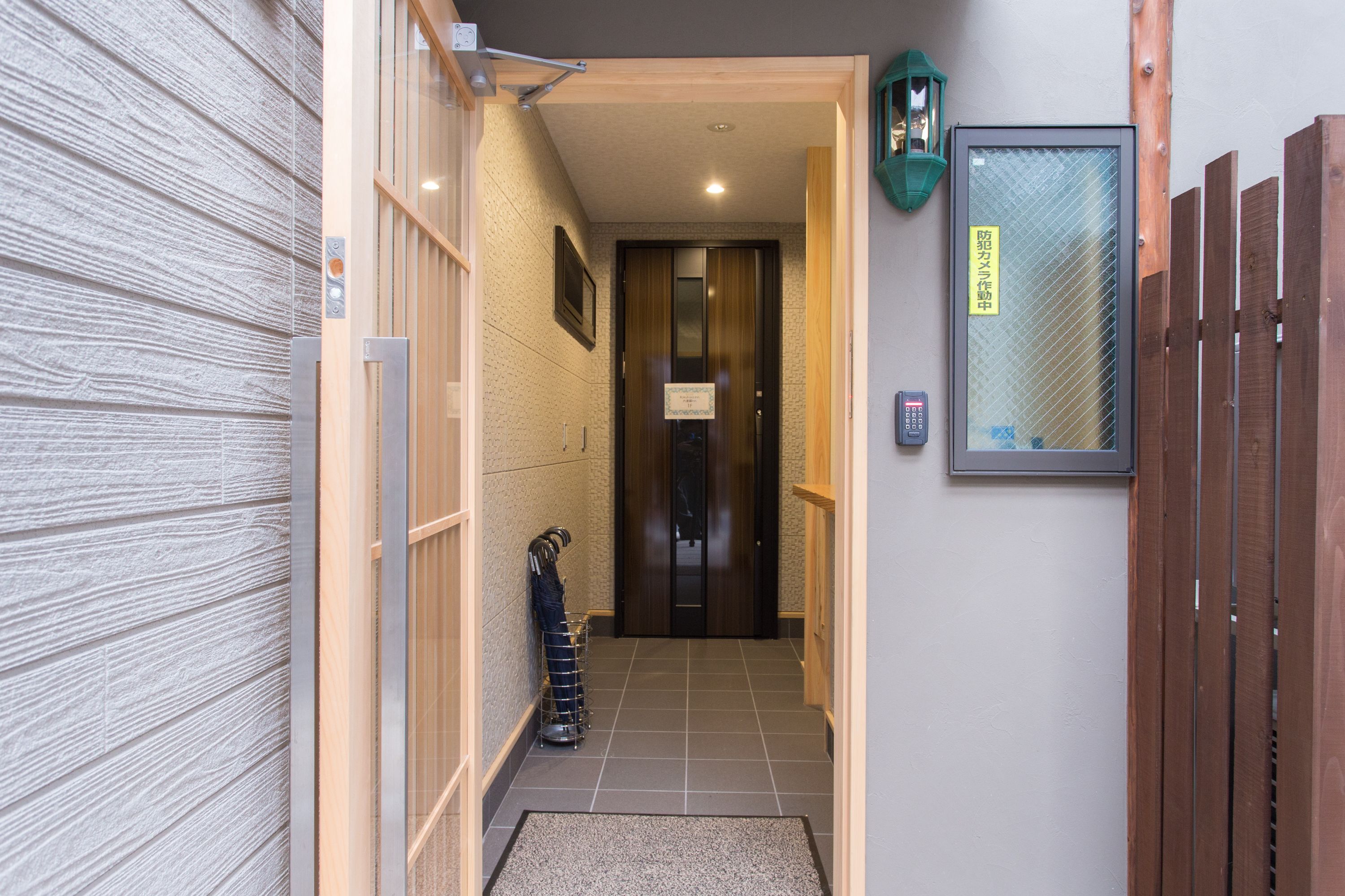 A narrow hallway with a wooden door at the end, a metal rack with items, and a small mat on the floor.