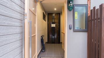 A narrow hallway with a wooden door at the end, a metal rack with items, and a small mat on the floor.