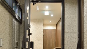 A hallway with a wooden door leading to a room with a tiled floor and a wooden shelf.