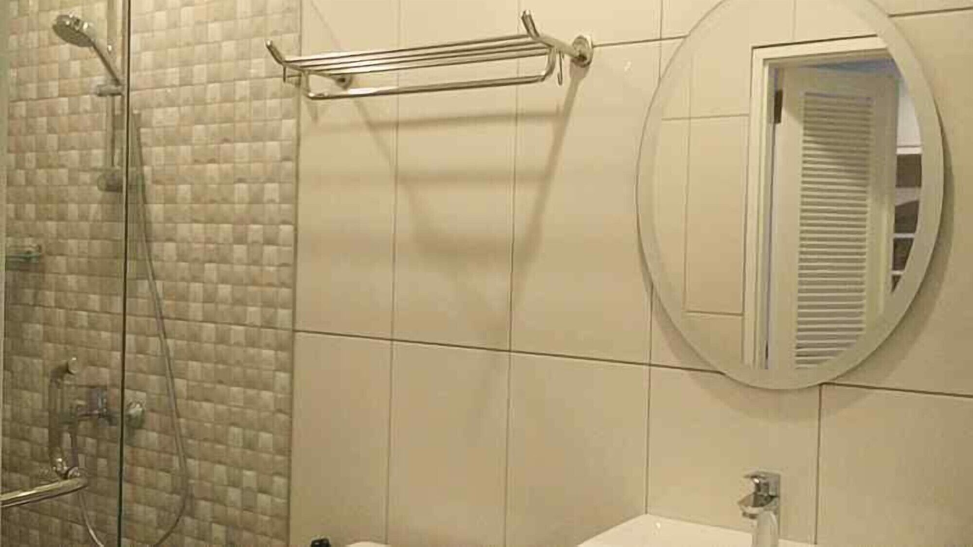A bathroom with a glass shower enclosure, a towel rack, and a round mirror.