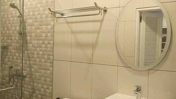 A bathroom with a glass shower enclosure, a towel rack, and a round mirror.