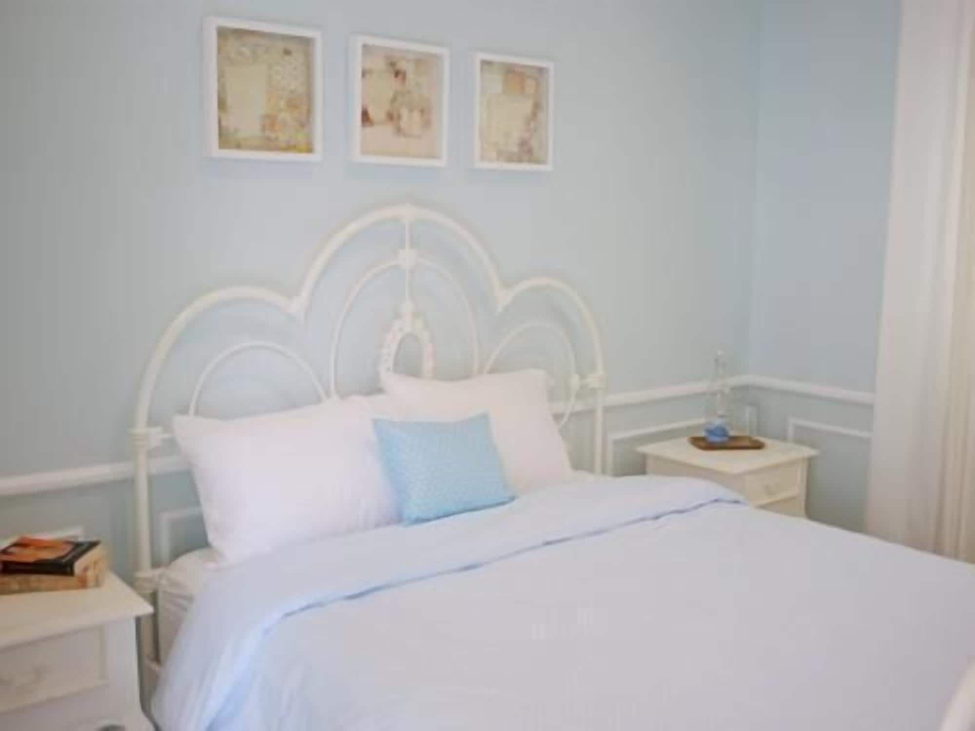 A bedroom with a white bed, a nightstand, and a wall with three framed pictures.