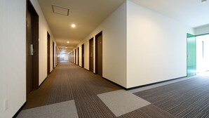 Een lange, smalle hotelgang met vloerbedekking en deuren aan beide zijden die naar kamers leiden.