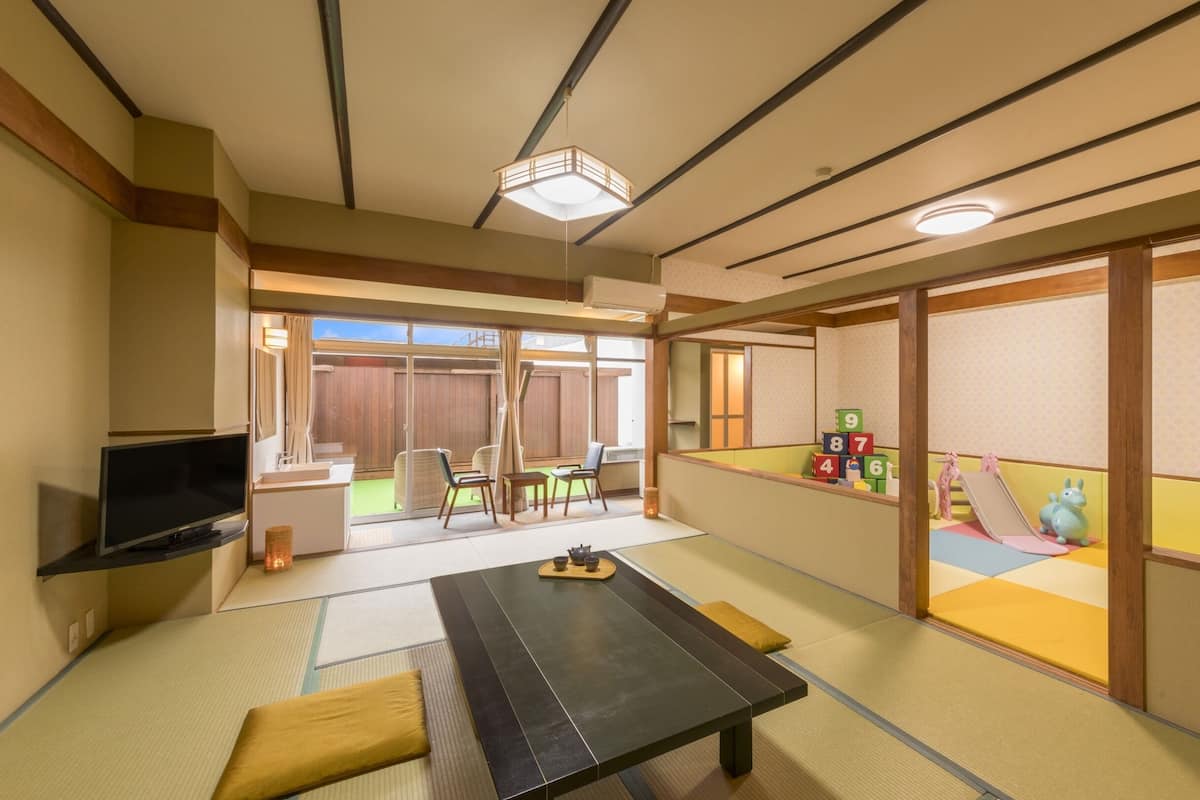 A traditional Japanese room with tatami flooring, a low table, sliding doors, and a TV.