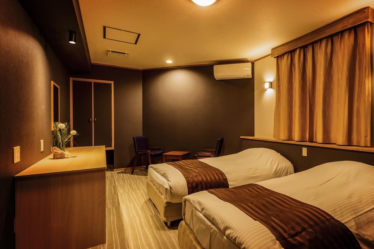 A hotel room with two beds, a desk, a chair, a mirror, and a window with curtains.