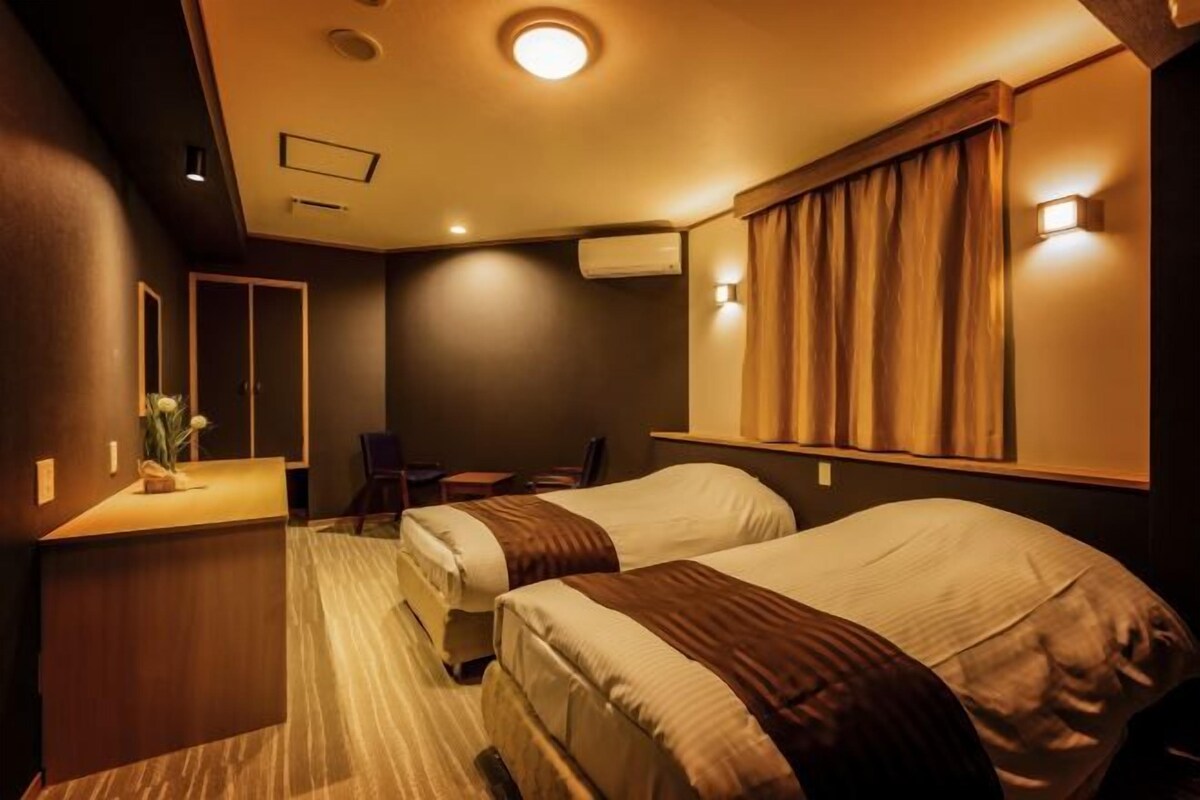 A hotel room with two beds, a desk, a chair, a mirror, and a window with curtains.