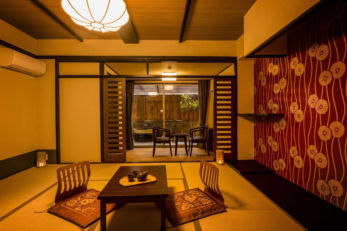 A traditional Japanese room with tatami flooring, a low table with a tea set, and sliding doors leading to a garden.