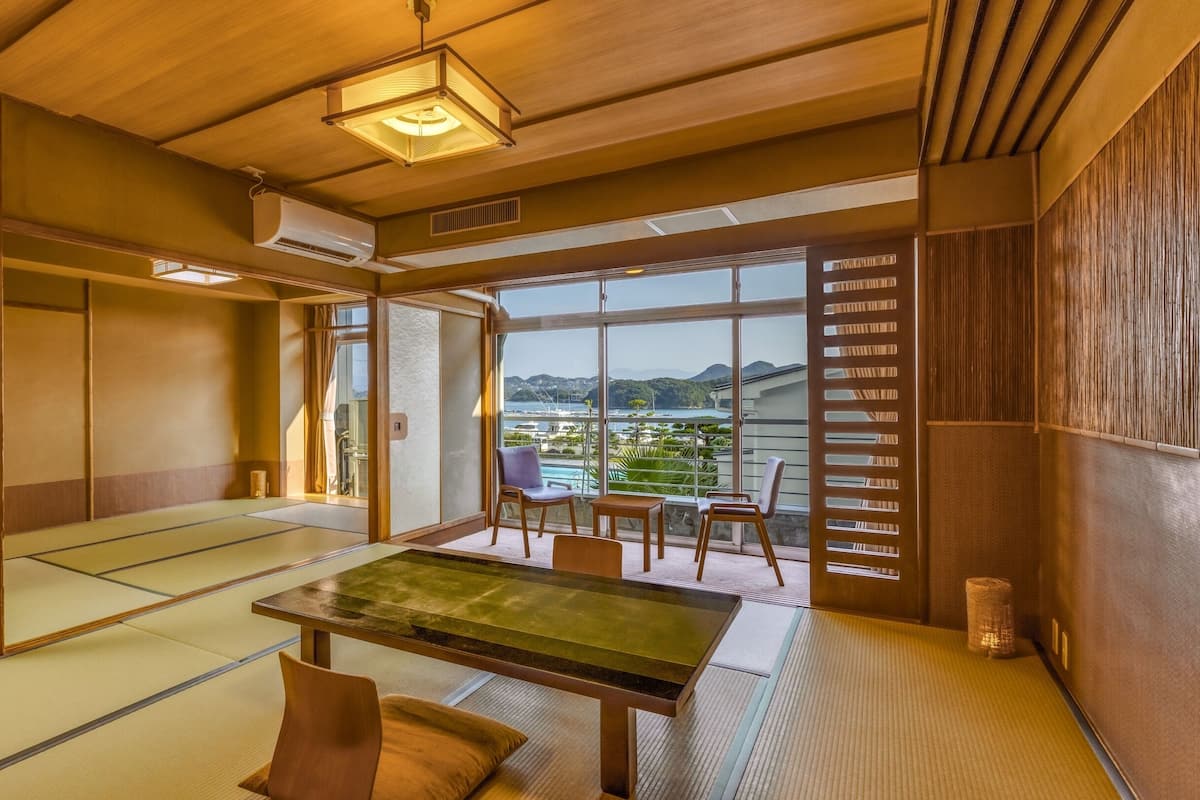 A traditional Japanese room with tatami flooring, a low table, and a view of a coastal landscape.
