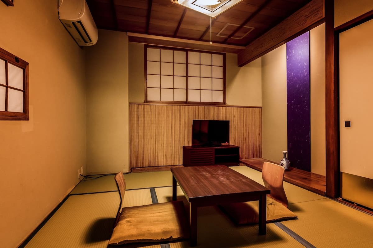 A traditional Japanese room with tatami flooring, a low wooden table, a television, and sliding doors.