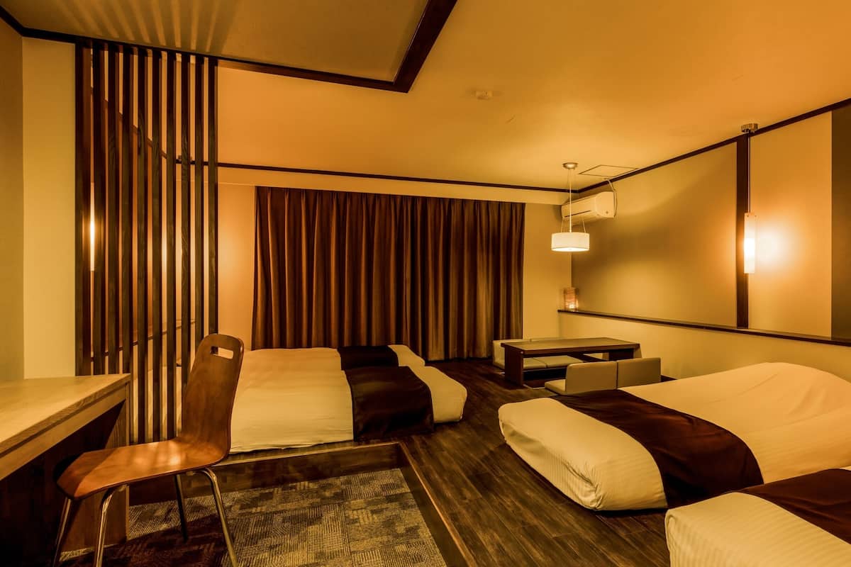 A hotel room with a bed, a desk, a chair, a small table, and a curtain.