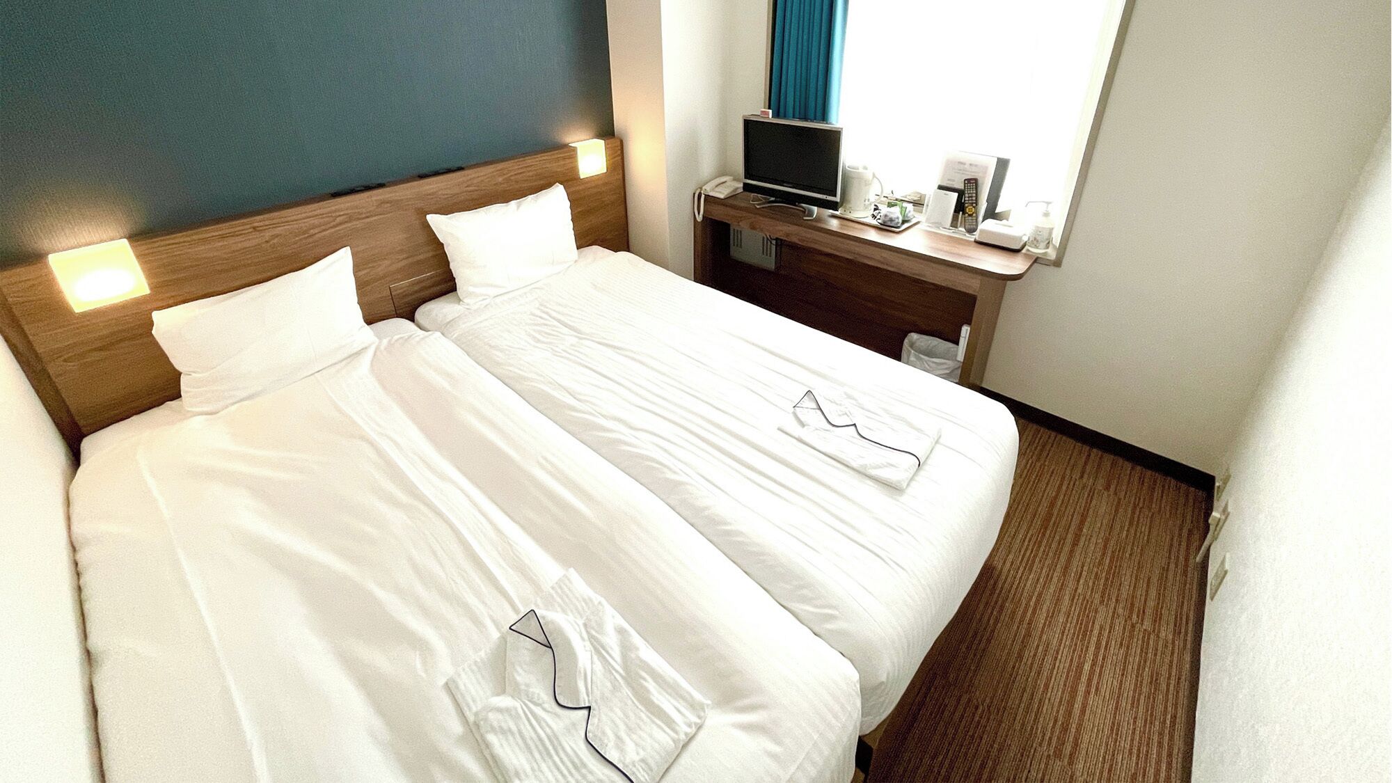 A hotel room with a double bed, bedside tables, a TV, and a window with curtains.
