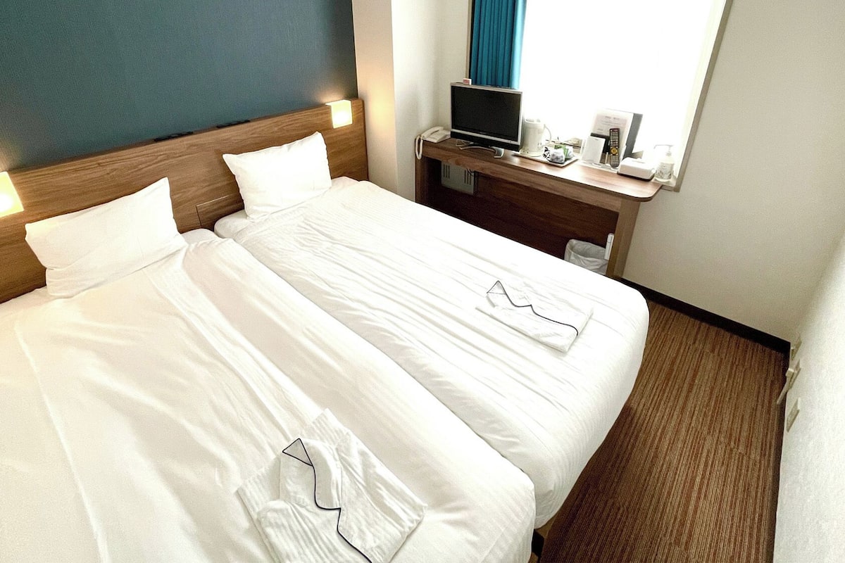 A hotel room with a double bed, bedside tables, a TV, and a window with curtains.