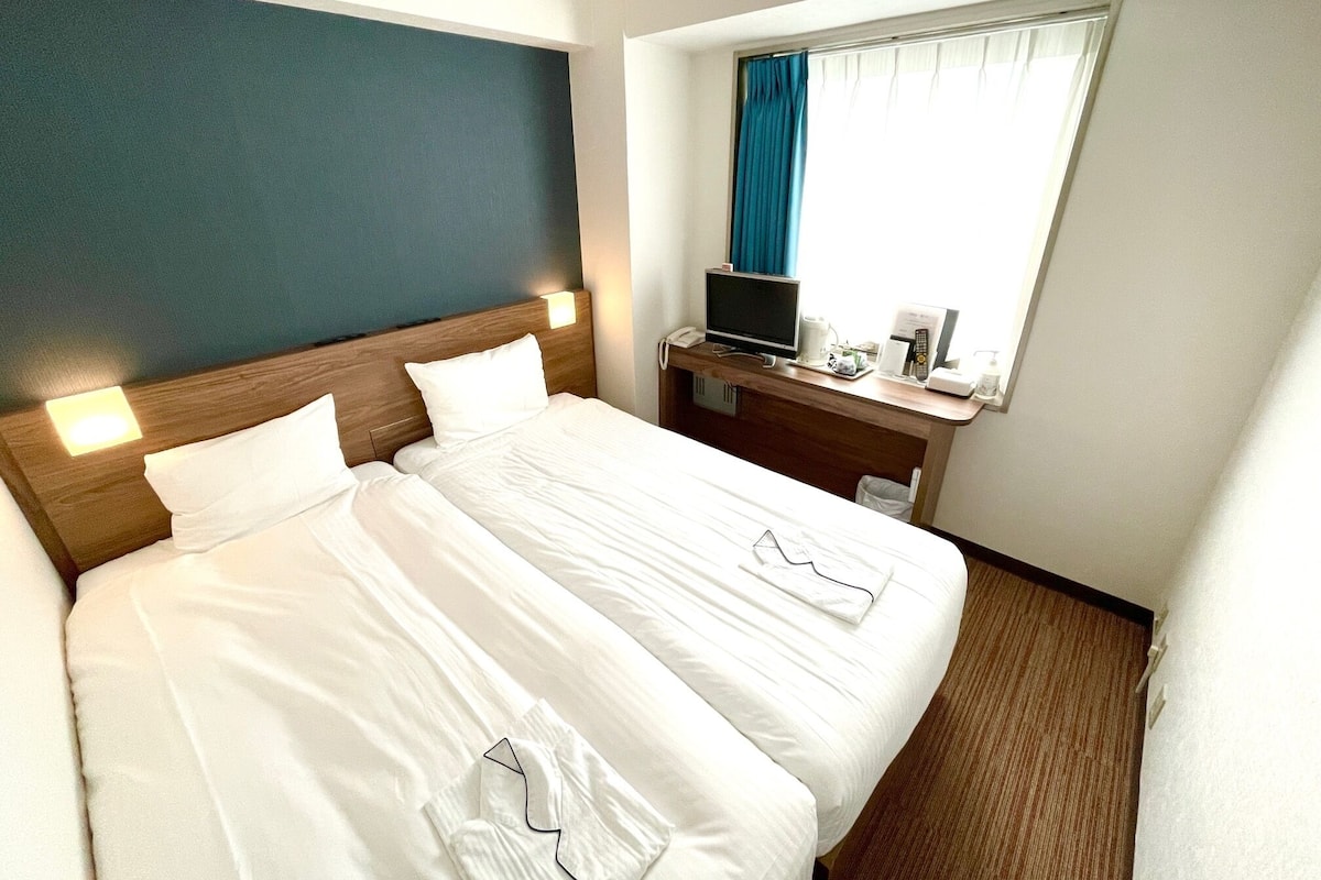 A hotel room with a large bed, a desk with a computer, and a window with curtains.