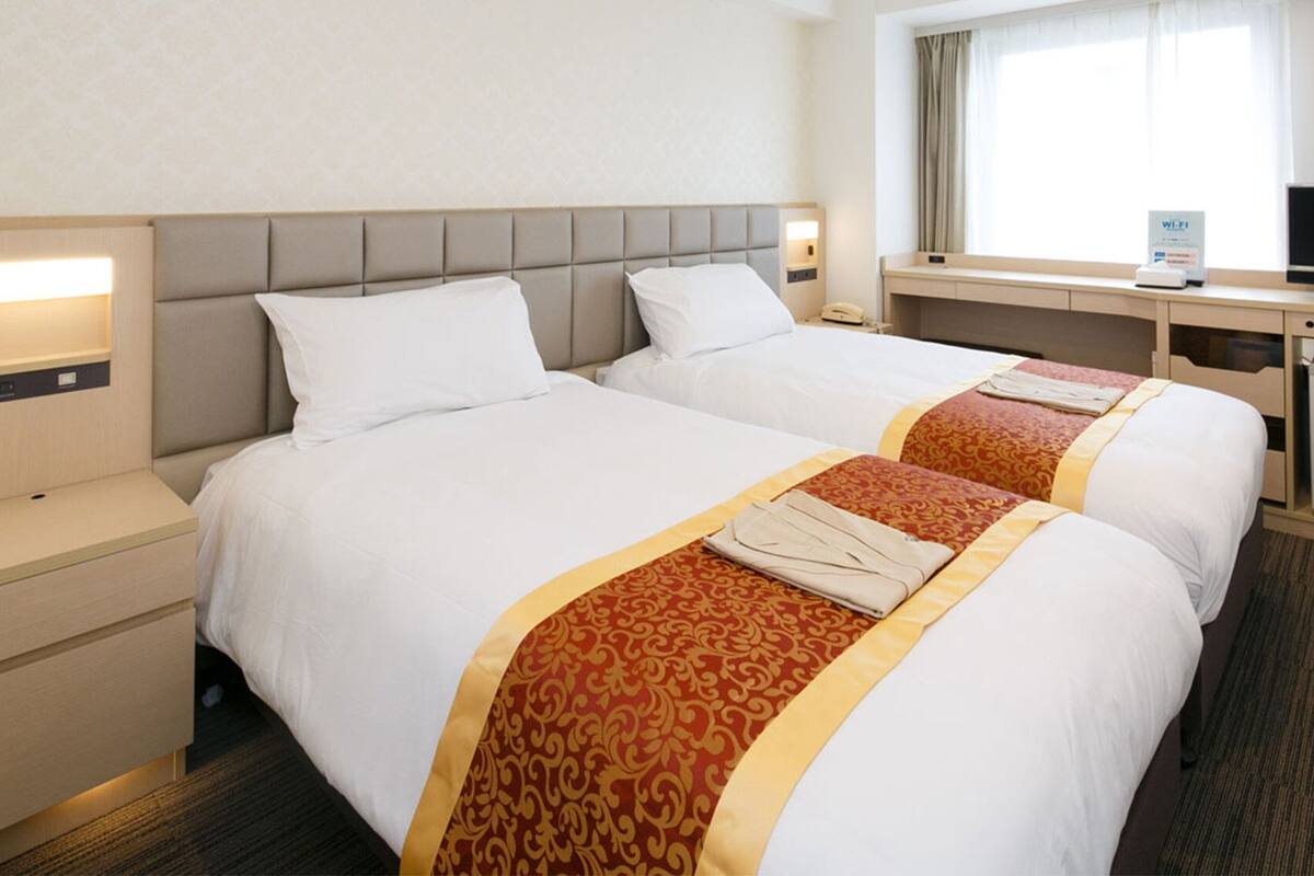 A hotel room with two beds, a desk, a television, and a refrigerator.