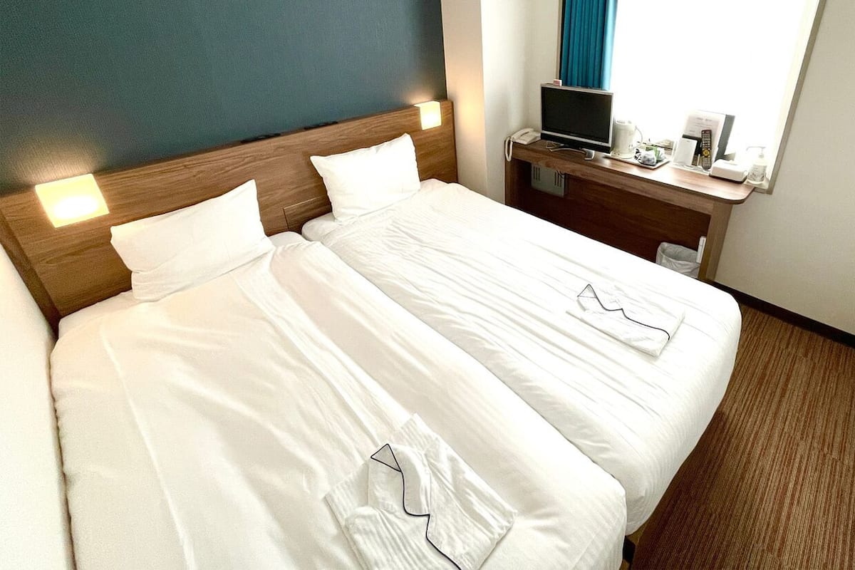 A hotel room with a large bed, a desk with a computer, and a window with curtains.