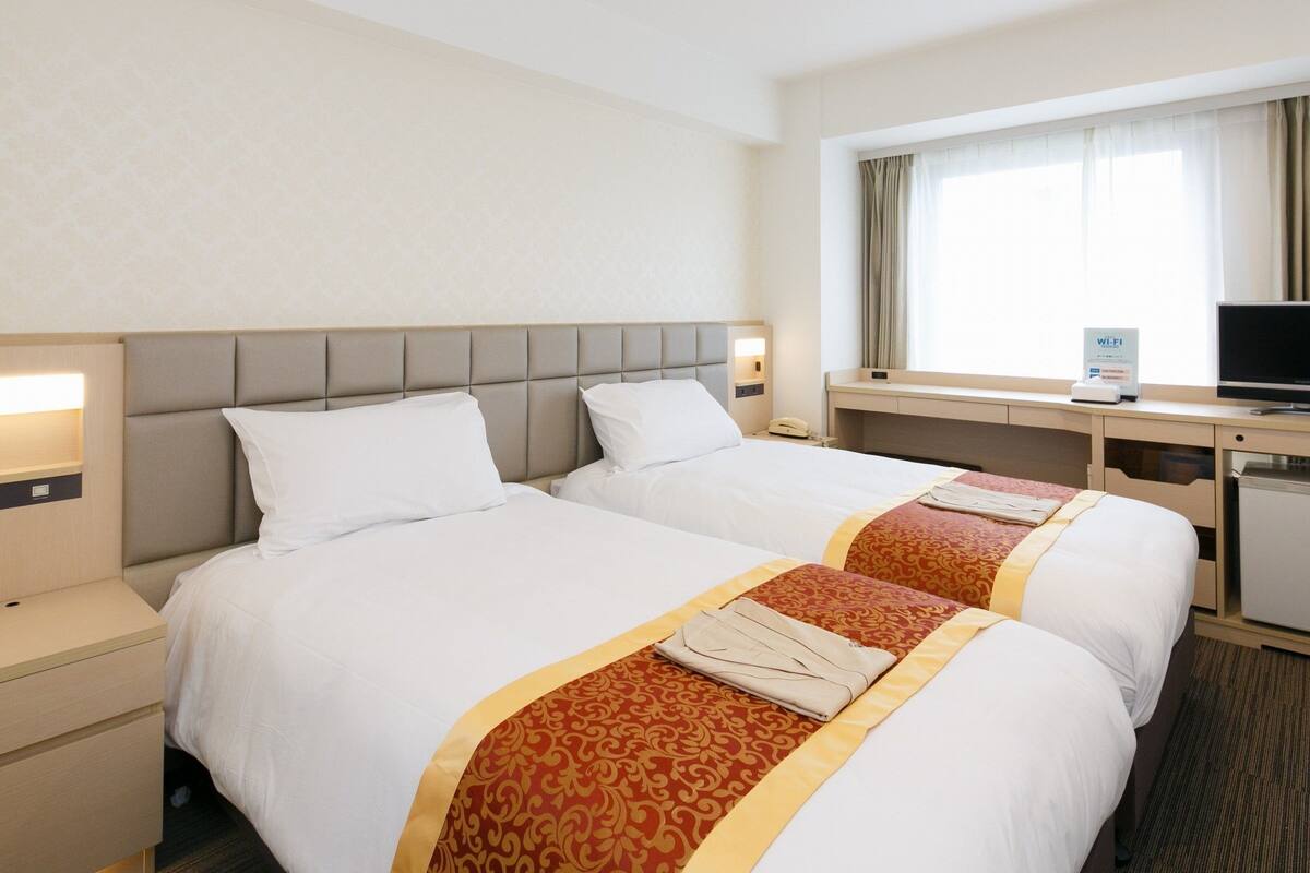 A hotel room with two beds, a desk, a TV, and a Wi-Fi sign.