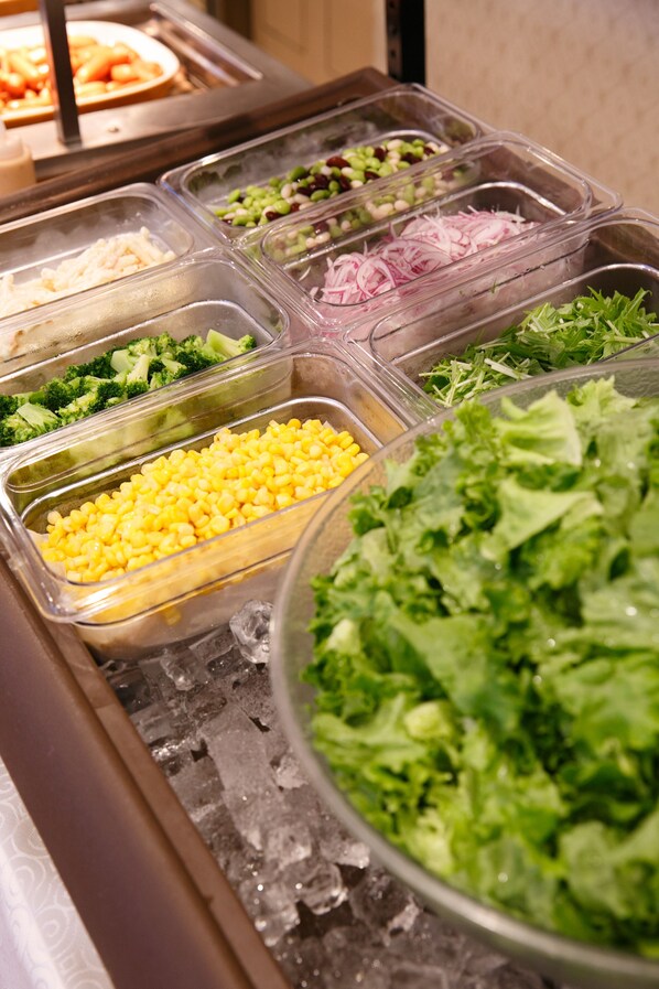 A buffet with various food options including corn, broccoli, and mixed greens.