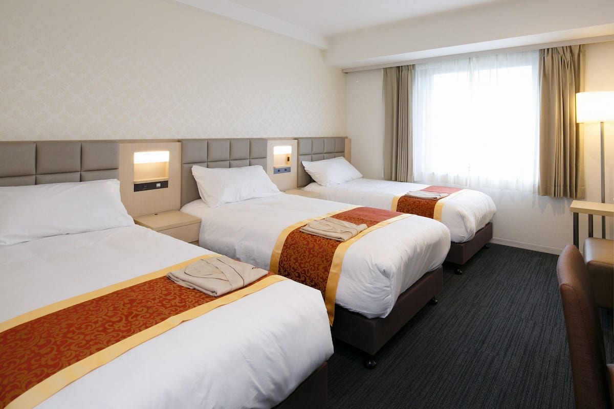 A hotel room with three single beds, each with a headboard, bedside tables, and lamps.