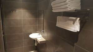 A modern bathroom with dark tiles, a sink, and a towel rack with folded towels.