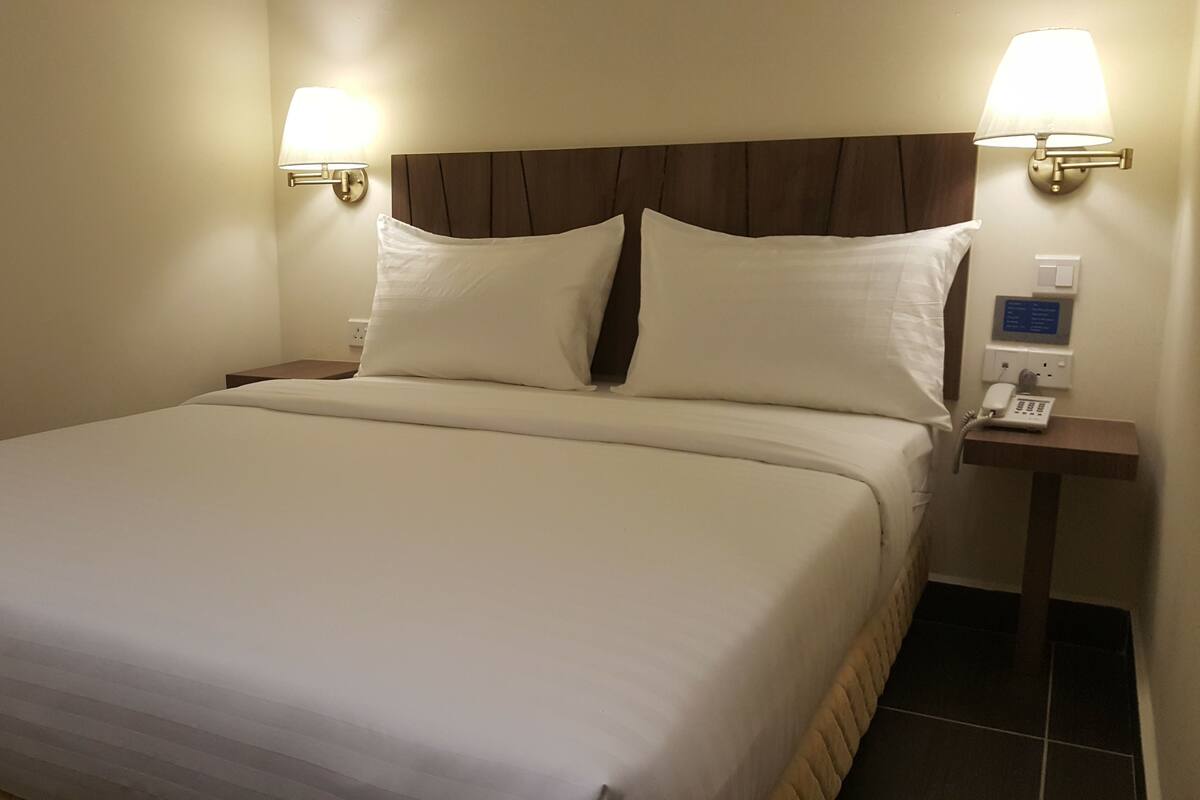 Una habitación de hotel con una cama grande, dos lámparas de noche, un teléfono junto a la cama y un panel de control en la pared.