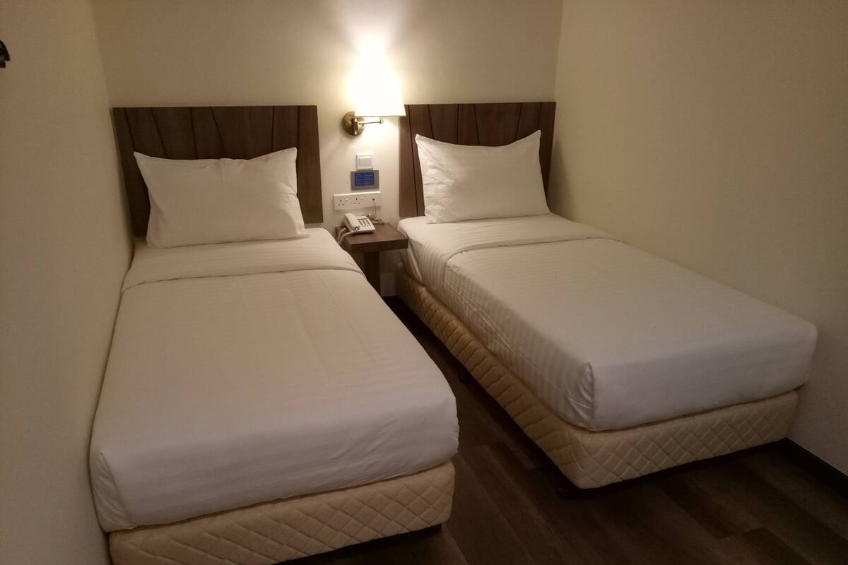Habitación de hotel con dos camas individuales, una mesita de noche con teléfono y una lámpara fijada a la pared.