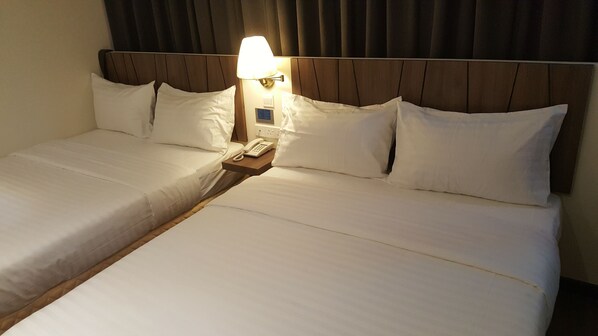 A hotel room with two beds, a nightstand with a lamp, and a phone.