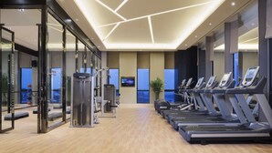 Une salle de sport moderne équipée de tapis de course, d’appareils de musculation et d’un grand miroir.