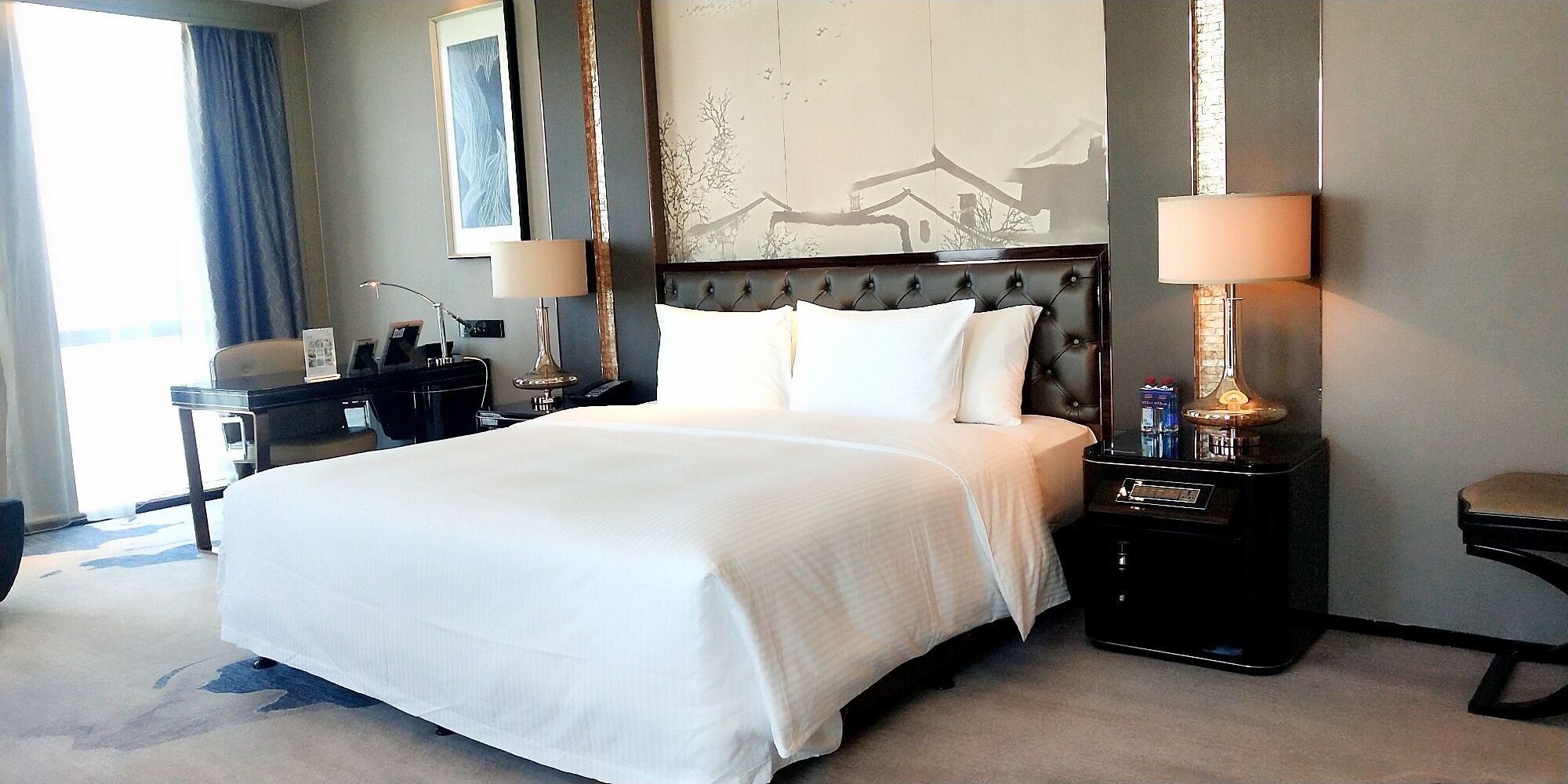 Una habitación de hotel con una cama grande, dos mesitas de noche con lámparas, un escritorio y una silla.