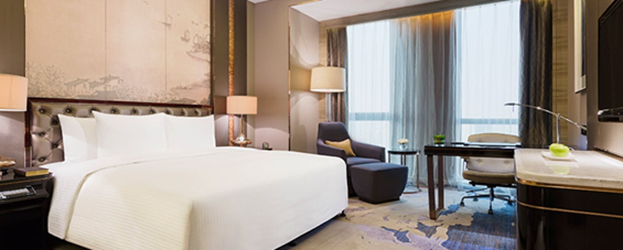Habitación de hotel con una cama grande, un escritorio con silla, una mesita y una lámpara.
