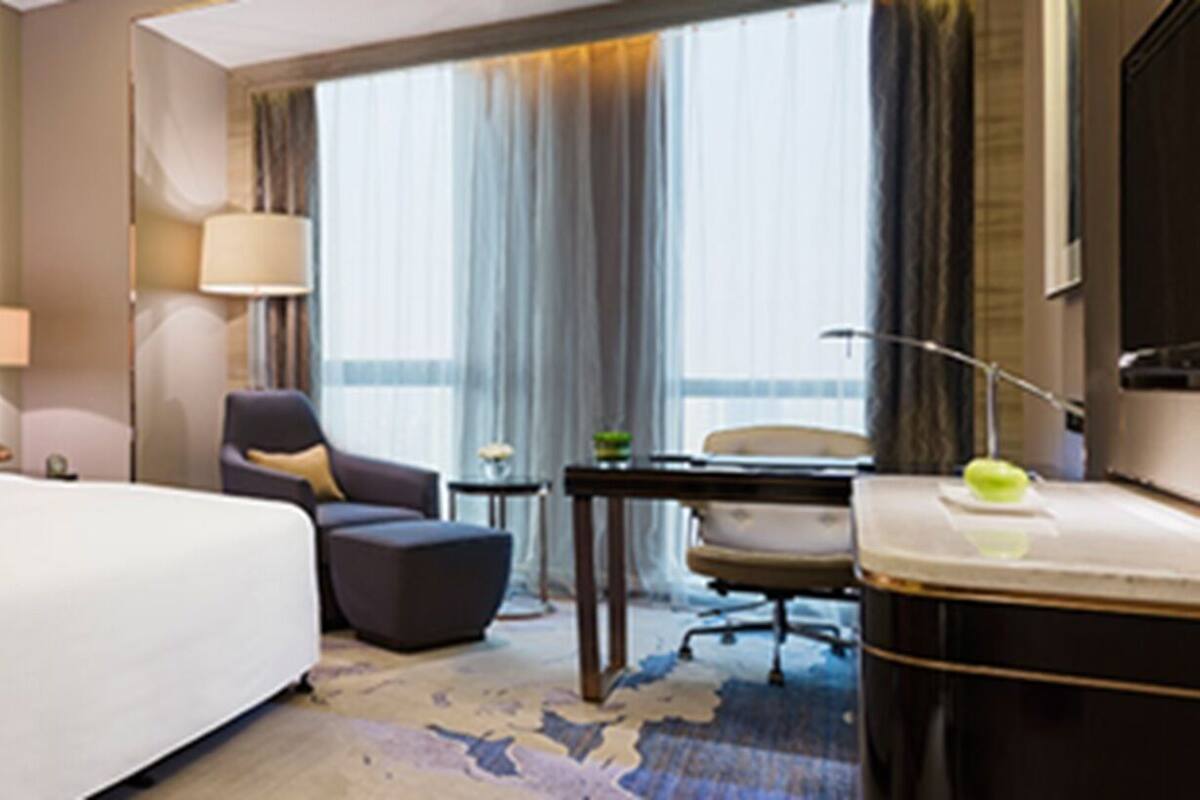 Habitación de hotel con una cama grande, un escritorio con silla, una mesita y una lámpara.