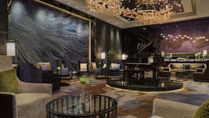 Un hall d’entrée luxueux agrémenté d’un grand piano, de fauteuils confortables, d’une grande fresque murale et d’un luminaire au plafond au design unique.