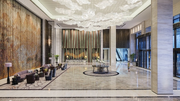 Un hall d’entrée spacieux, agrémenté d’un lustre moderne, d’un coin salon et d’une grande fenêtre offrant une vue sur l’extérieur.