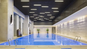 Une piscine intérieure moderne, avec de l’eau cristalline, entourée de chaises longues et de plantes en pot.