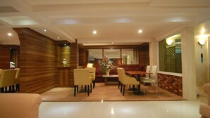 A modern dining area with a wooden accent wall, a central dining table with chairs, and a large window providing natural light. - Grand Kasira (Jakarta)