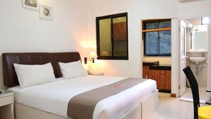 A hotel room with a bed, bedside table, lamp, and a bathroom visible through an open door. - Grand Kasira (Jakarta)