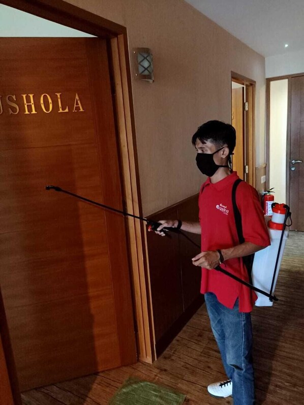 A person in a red shirt holding a device near a wooden door with 'USHOLA' written on it. - Grand Kasira (Jakarta)