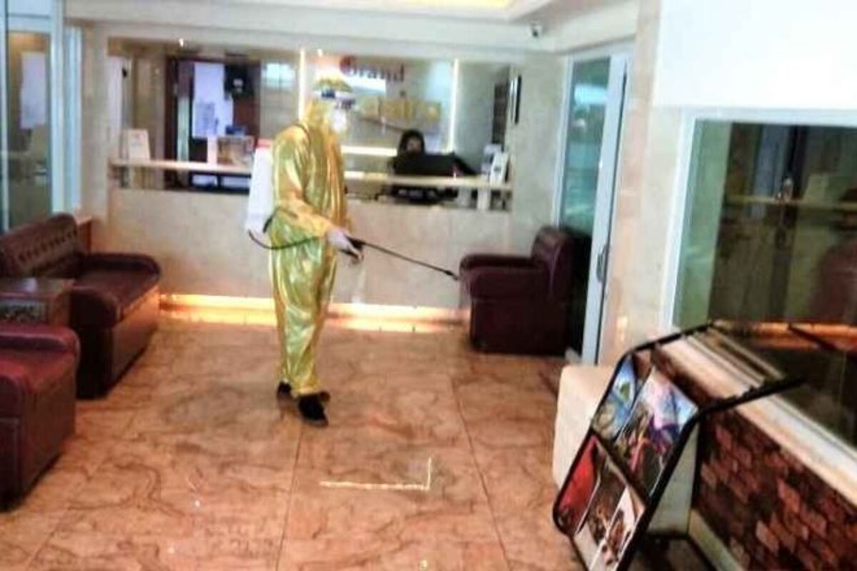 Una persona con traje dorado limpiando un vestíbulo con una aspiradora. Se observan sofás rojos y un mostrador de recepción al fondo.