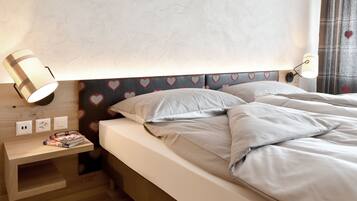A neatly made bed with a headboard featuring heart patterns, a bedside table with a lamp, and a small shelf with books.