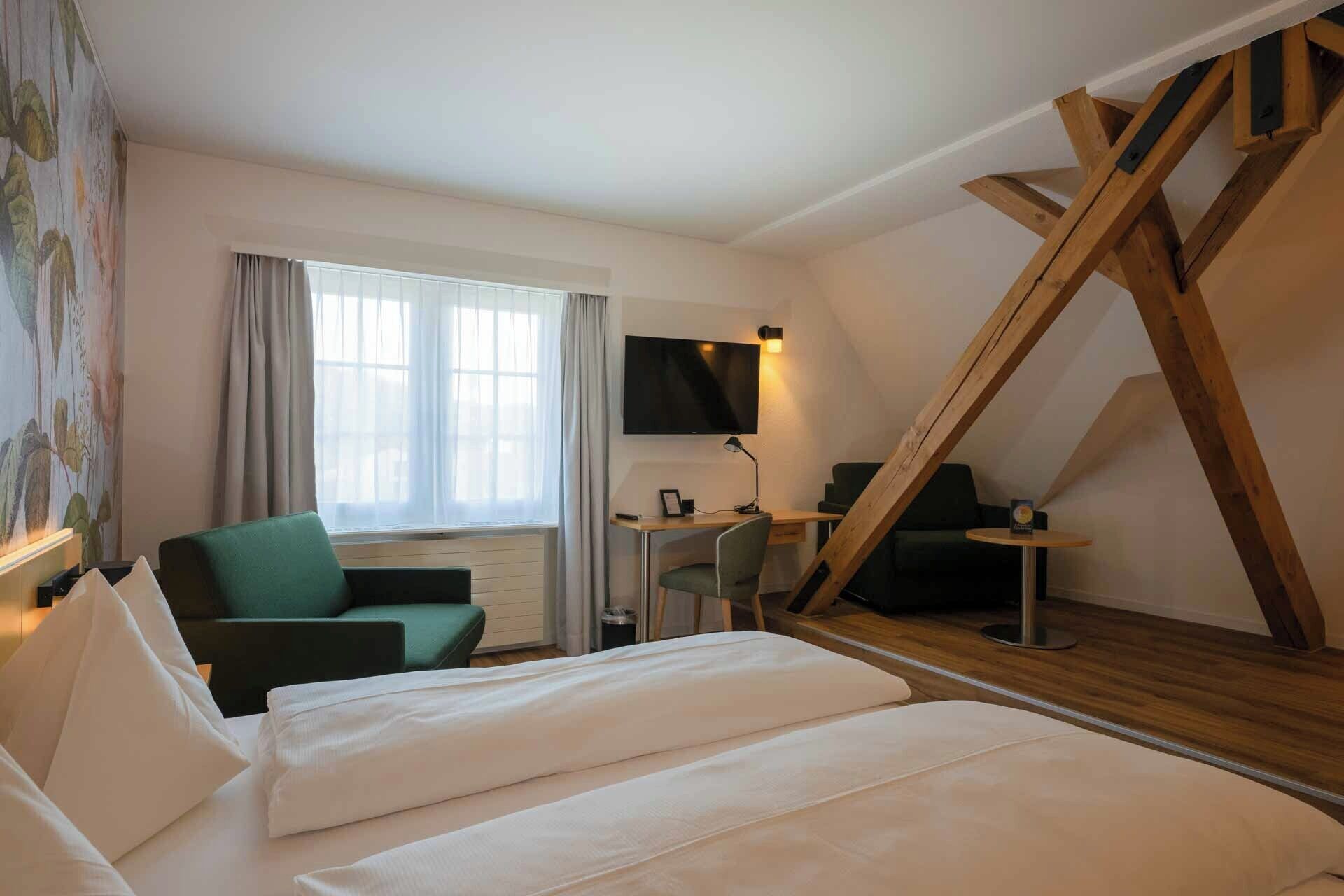 Una habitación de hotel con una cama, un escritorio con una silla, un televisor y una escalera.