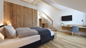 A bedroom with a wooden headboard, a bed with pillows, a desk with a chair, a TV, and a staircase.
