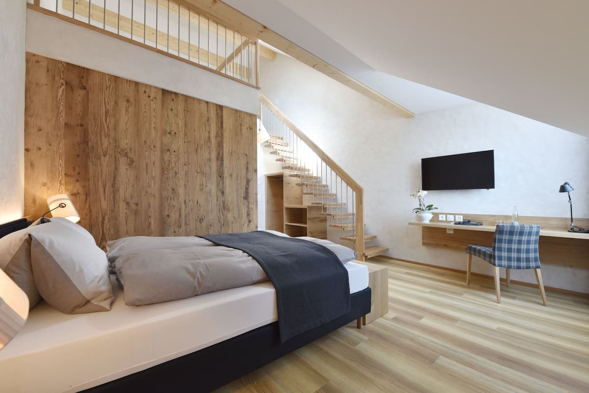 Een slaapkamer met een houten hoofdbord, een bed met kussens, een bureau met stoel, een televisie en een trap.