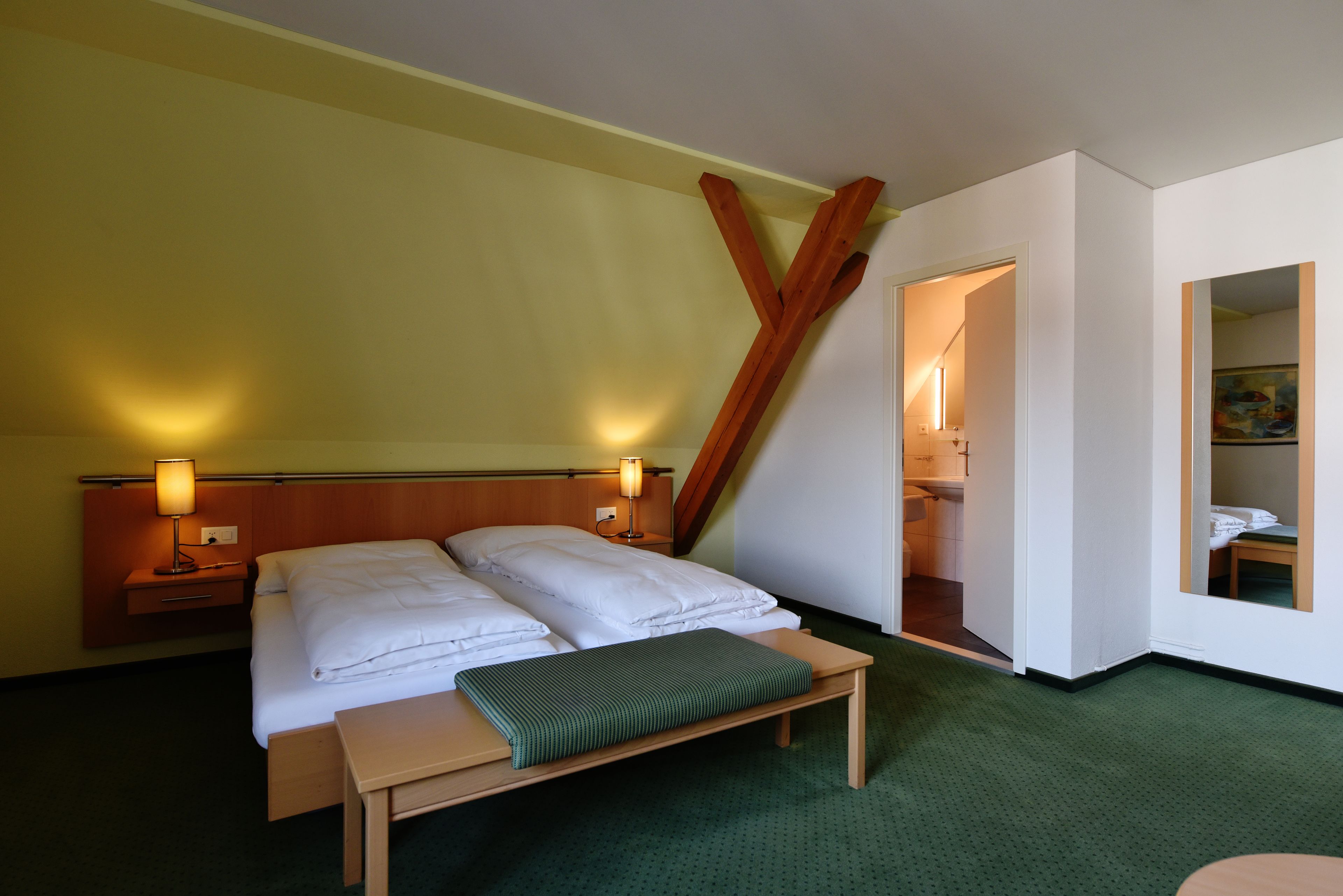 A hotel room with a bed, bedside tables, a bench, and a painting on the wall.