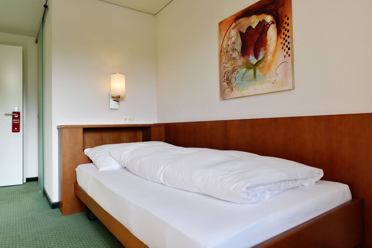 Een hotelkamer met een houten bed, witte beddengoed, een wandlamp en een schilderij.