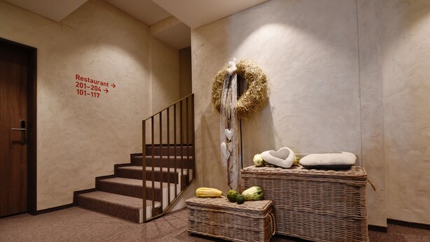 Un hall d’hôtel avec un escalier, un panneau indiquant l’emplacement des restaurants et un mur décoratif orné d’une guirlande et de coussins.