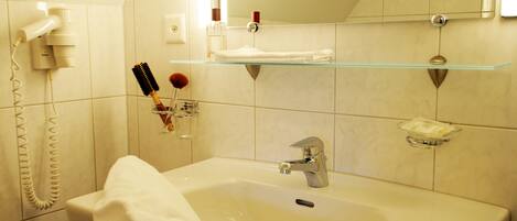 Un baño con lavamanos, espejo y repisa de vidrio encima del espejo.