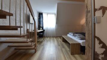 A modern room with a wooden staircase, a desk with a chair, a bed, and a window with curtains.