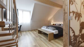 A modern bedroom with a sloped ceiling, a wooden staircase, a bed with a bench, and a desk.